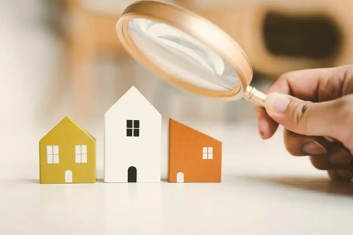 Lente d'ingrandimento esamina tre casette di legno, evidenziando la differenza tra cessione e subentro nel mercato immobiliare.