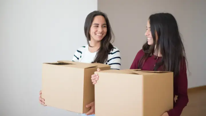 Due amiche sorridenti trasportano scatoloni, pronte per il precetto rilascio immobile prima della scadenza.